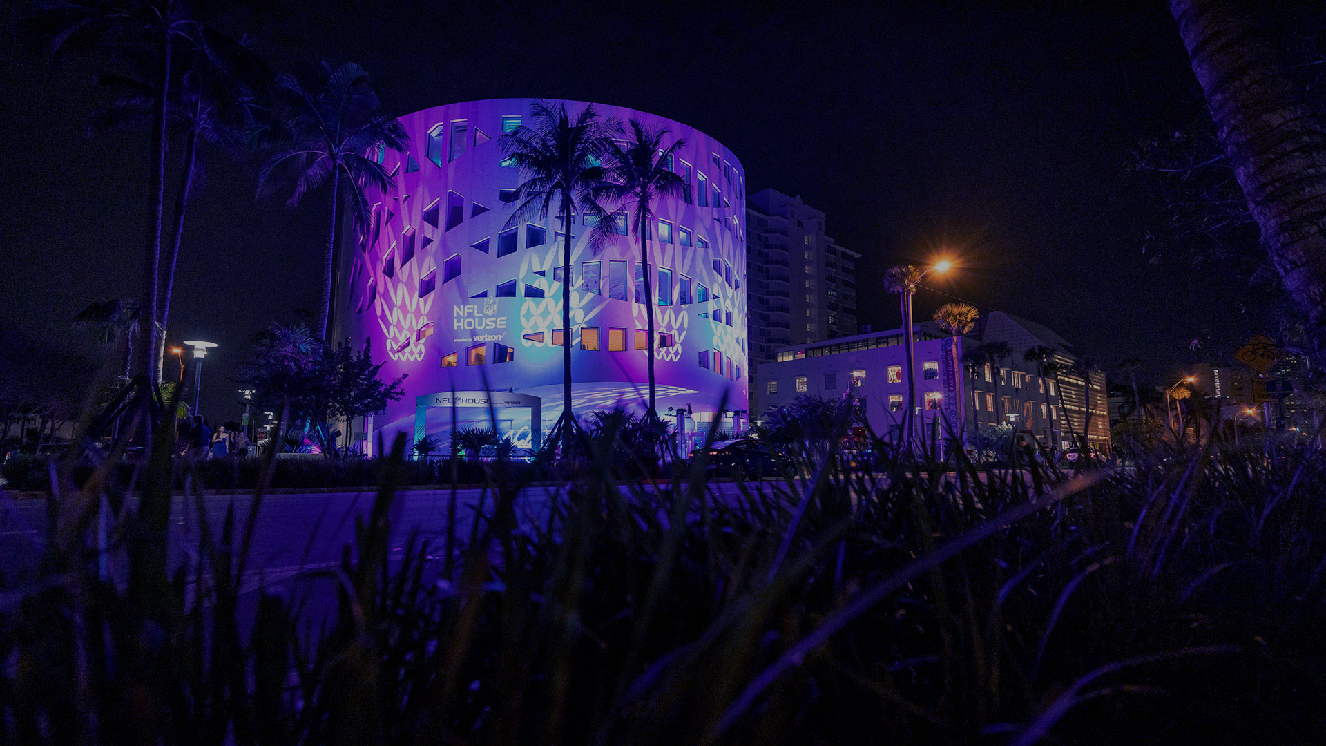 An outside view of NFL Super Bowl VIP Experience. The circular building glows at night.  